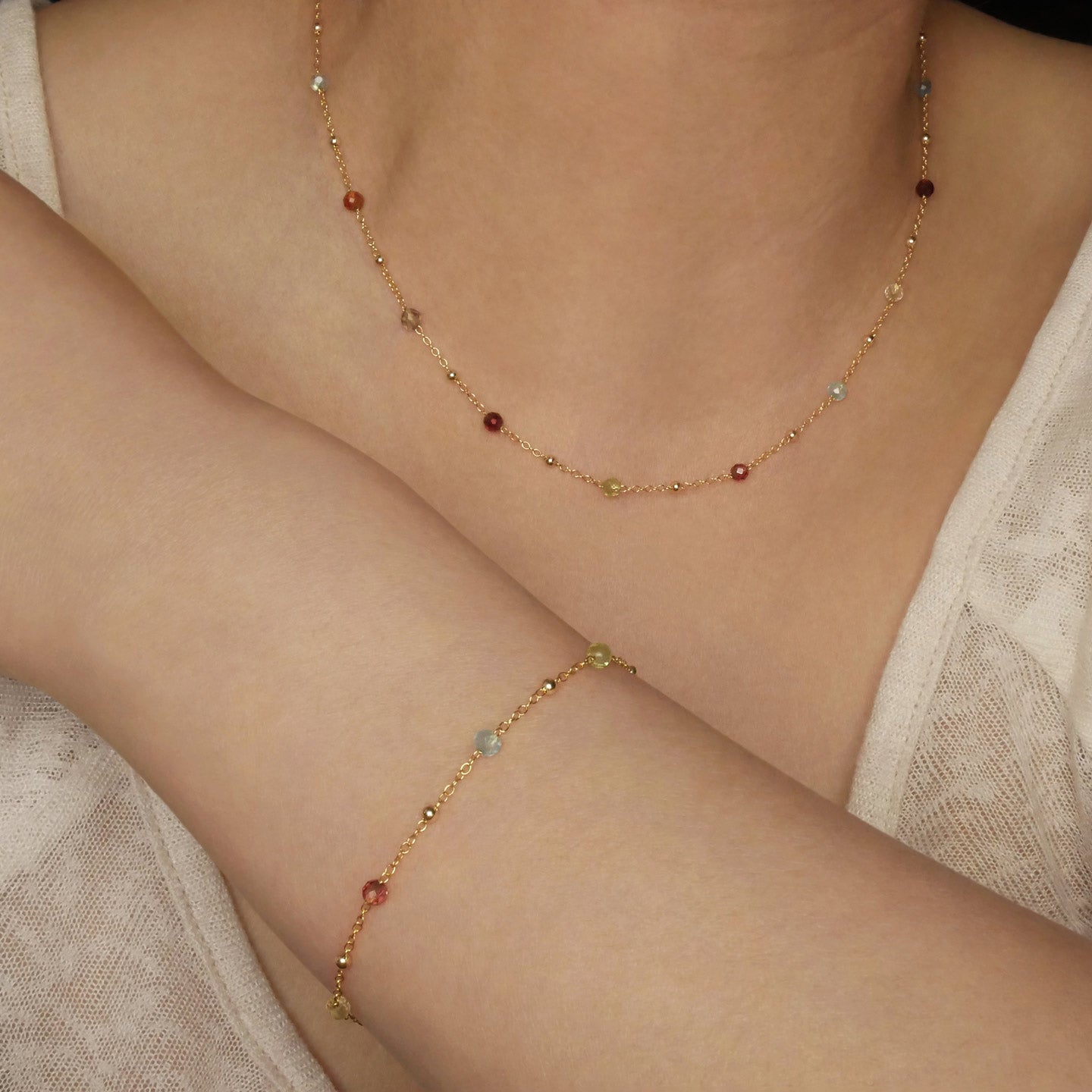 Estelle dainty high quality natural multi-colored gemstone beaded chain adjustable necklace and bracelet in 14K gold filled, shown worn on a model’s neck and wrist. Featuring high quality AAA Apatite, Agate, Citrine, Garnet, Labradorite, Obsidian, Peridot gemstones.