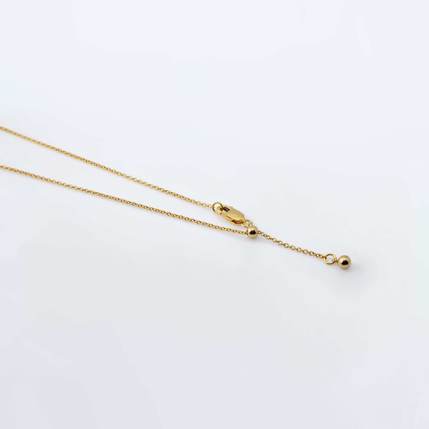Dainty adjustable 14k gold filled chain necklace. It shows the ends of the adjustable area, ball and clasp laying flat on a plain white background.