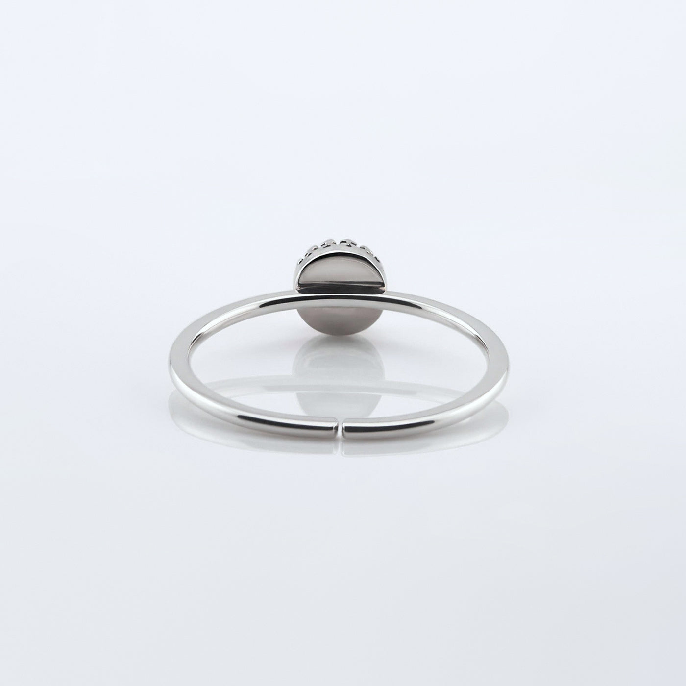Back view of a dainty adjustable sterling silver ring with a focal crown bezel setting. The ring is laying flat on a plain white reflective surface.