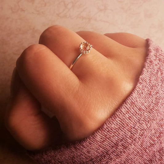 Close-up of a hand wearing a dainty adjustable sterling silver ring with a focal strawberry quartz solitaire gemstone cabochon, set in a crown bezel setting. The person had a soft pink textured long sleeve sweater over the hand.