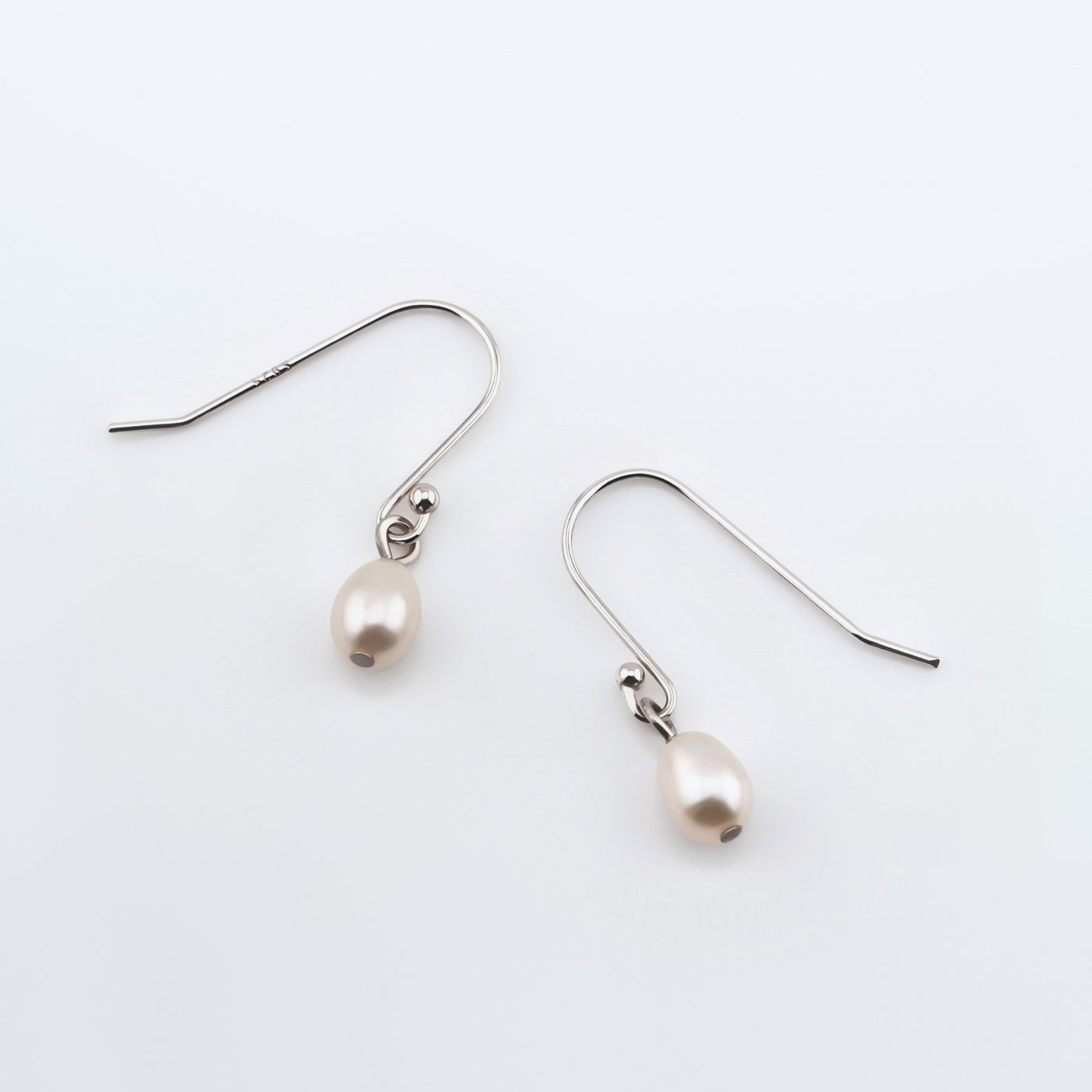 Pearl drop French hook earrings on plain white background, top view.