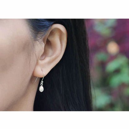 Close-up of a model's ear wearing Pearl drop French hook sterling silver earrings with a blurred flower outdoor background.