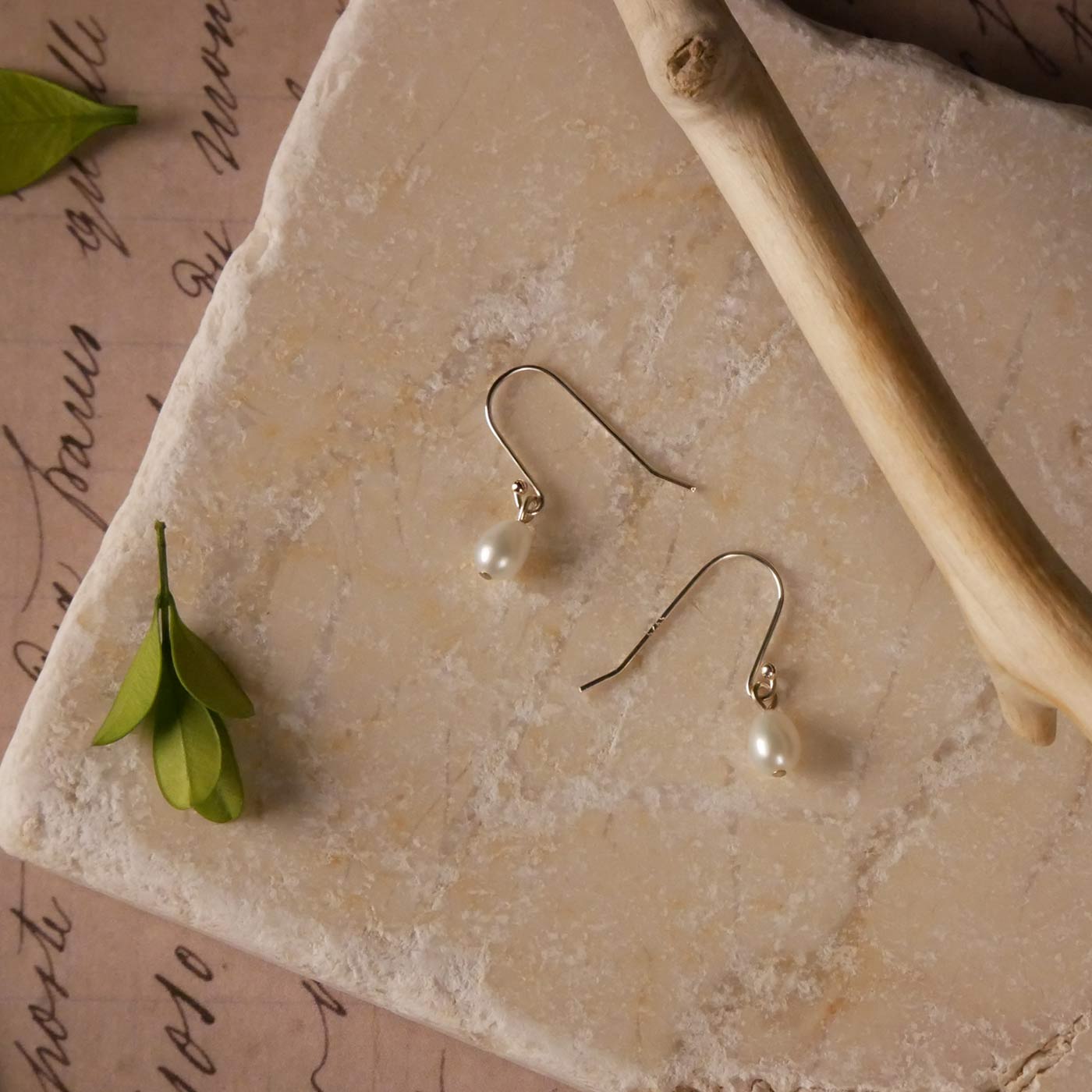 Pearl drop French hook sterling silver earrings on a stone surface stylized with  branch and leaves as accents.