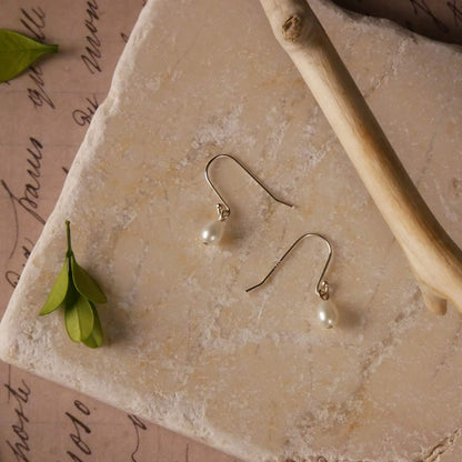 Pearl drop French hook sterling silver earrings on a stone surface stylized with  branch and leaves as accents.