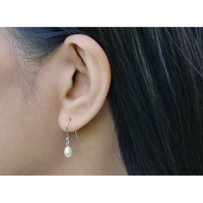 Close-up of Pearl drop French hook sterling silver earrings on a model's ear, with dark hair in the background