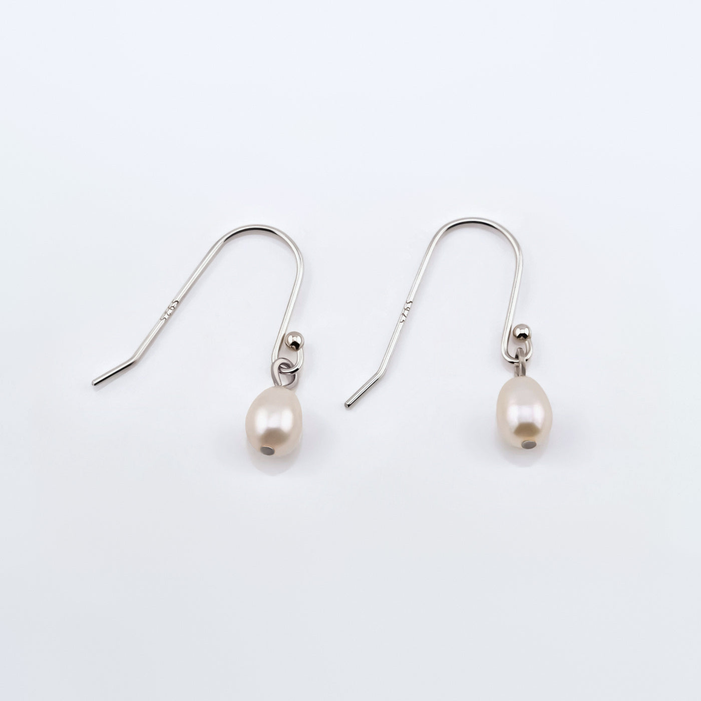 Pair of Pearl drop French hook sterling silver earrings on a plain white background, top view.