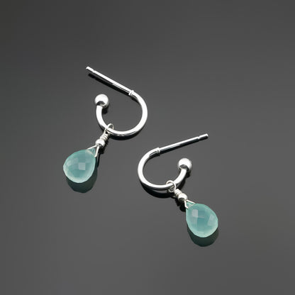 Top view of a pair of mini sterling silver hoop earrings with aqua blue-green teardrop-shaped AAA quality chalcedony gemstones on a dark gray background, top view.