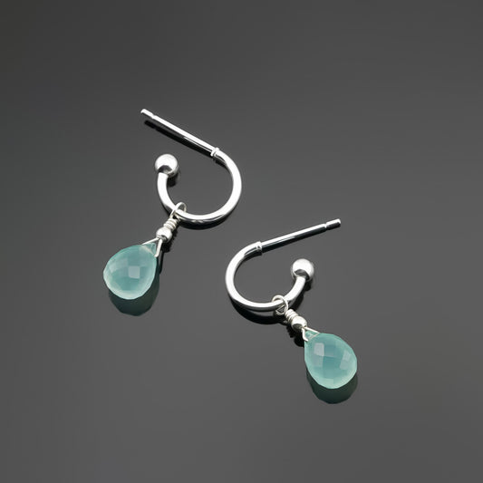 Top view of a pair of mini sterling silver hoop earrings with aqua blue-green teardrop-shaped AAA quality chalcedony gemstones on a dark gray background, top view.