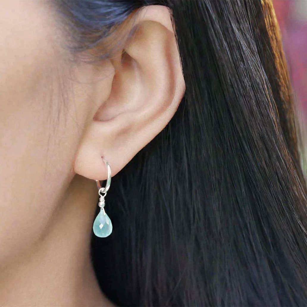 Close-up of a person's ear wearing a sterling silver mini hoop earring with a blue-green teal high quality AAA aqua chalcedony briolette drop shaped gemstone.