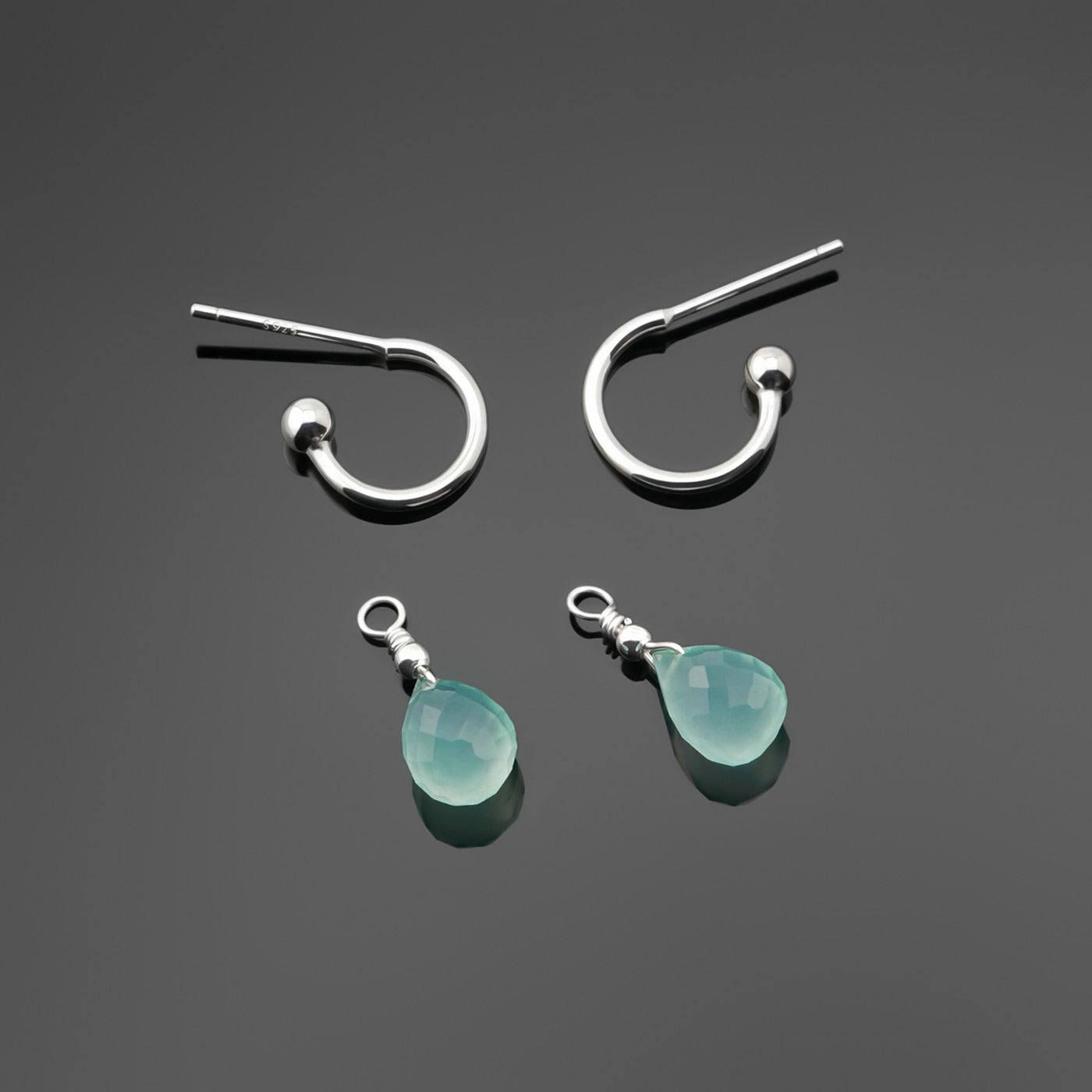 Sterling silver interchangeable mini hoop earrings, with blue-green teal aaa high quality aqua chalcedony teardrop shaped briolette gemstone charms on a dark gray plain background, top view.
