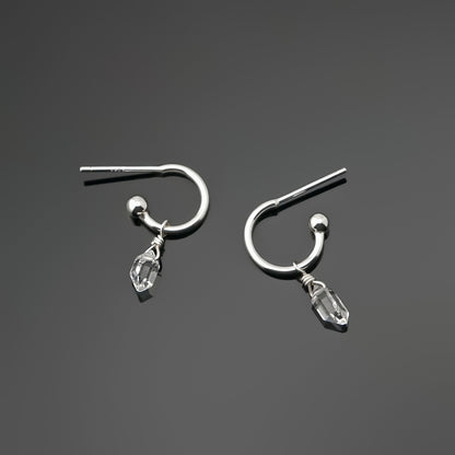 Pair of dainty high quality Herkimer Diamond Quartz drops on Sterling Silver hoop earrings laying on a dark gray background, top view.