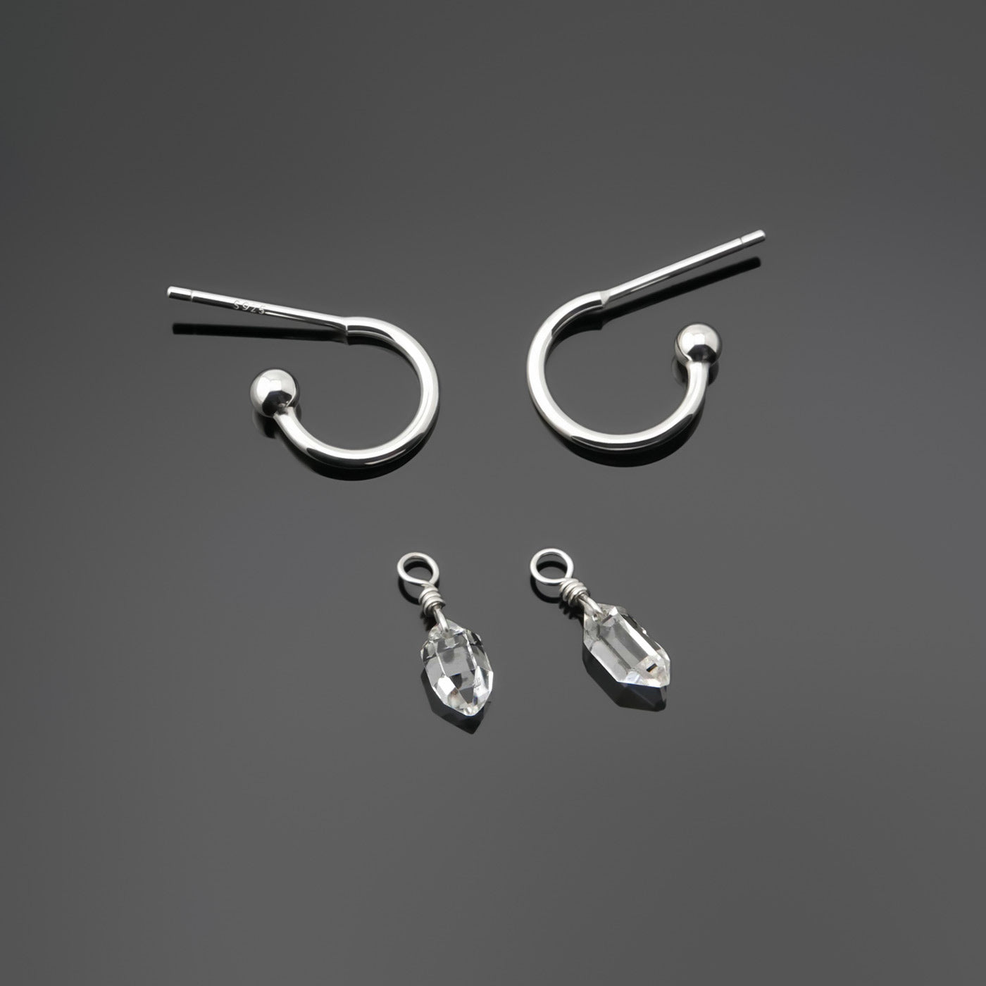 Pair of detachable, dainty high quality Herkimer Diamond Quartz drops  and Sterling Silver hoop earrings laying flat separately on a dark gray background, top view.