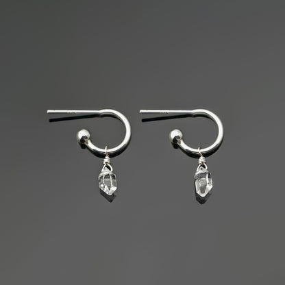 Pair of dainty high quality Herkimer Diamond Quartz drops on Sterling Silver hoop earrings laying on a dark gray background, top view.