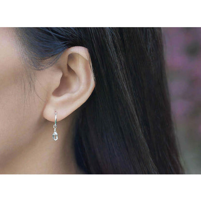 Dainty, high quality Herkimer Diamond Quartz drop on Sterling Silver hoop earring, worn outside by a person with long, dark hair and plants and flowers blurred in the background.