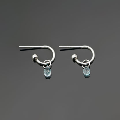 A pair of blue topaz gemstone sterling silver interchangeable hoop earrings, laying flat on a dark gray background, top view.
