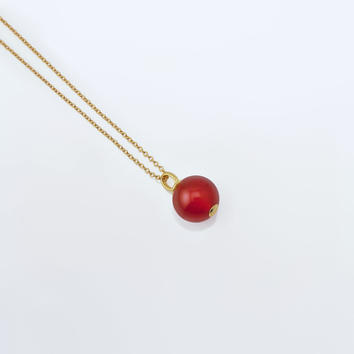 Top 3/4 view of a dainty round red carnelian ball sphere pendant necklace in 14k gold plated 925 sterling silver on a 14k gold filled chain, laying flat on a plain white background.  