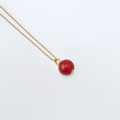 Top 3/4 view of a dainty round red carnelian ball sphere pendant necklace in 14k gold plated 925 sterling silver on a 14k gold filled chain, laying flat on a plain white background.  