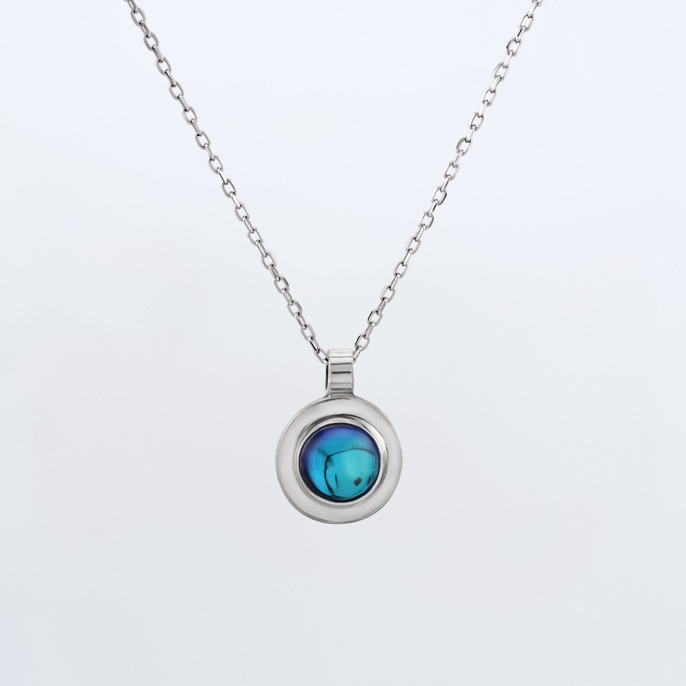 Front view of a dainty round Azotic blue topaz cabochon pendant 925 sterling silver necklace hanging, with a plain white background. 