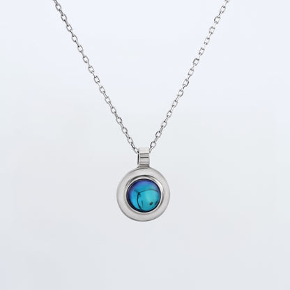 Front view of a dainty round Azotic blue topaz cabochon pendant 925 sterling silver necklace hanging, with a plain white background. 