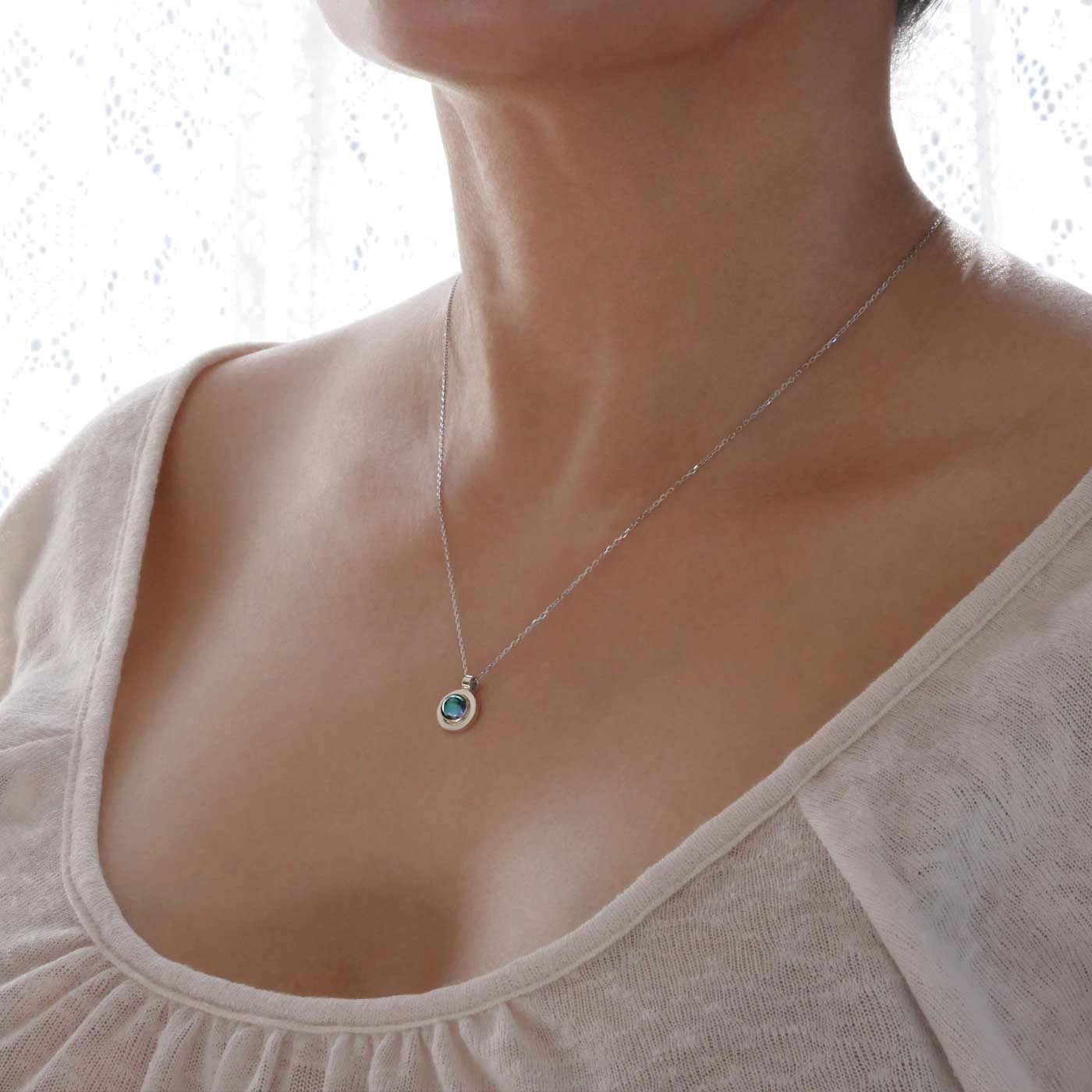 3/4 view of a dainty, round Azotic blue topaz cabochon pendant sterling silver necklace, worn by a person wearing a light beige shirt.