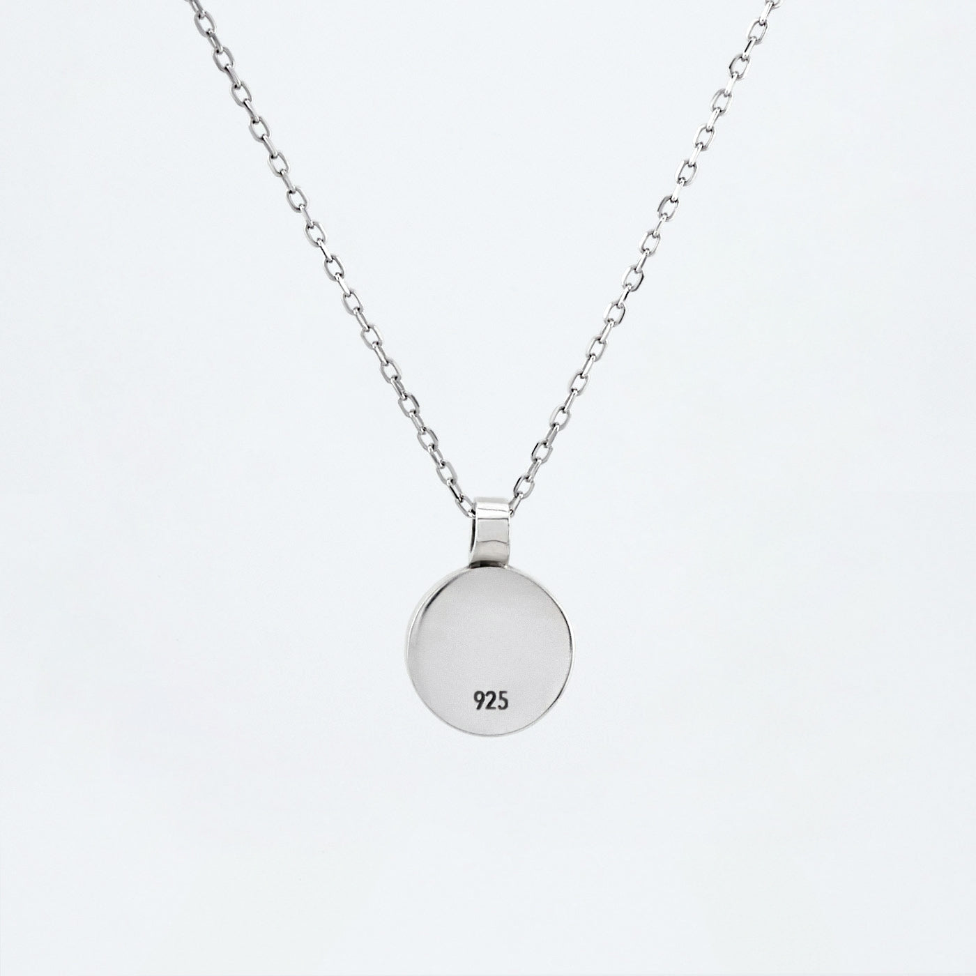 Back view of a dainty round Azotic blue topaz cabochon pendant sterling silver necklace hanging hallmarked 925, with a plain white background.