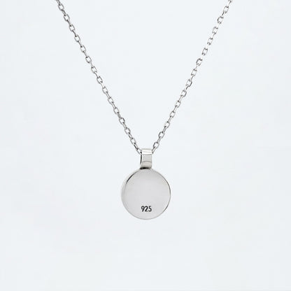 Back view of a dainty round Azotic blue topaz cabochon pendant sterling silver necklace hanging hallmarked 925, with a plain white background.