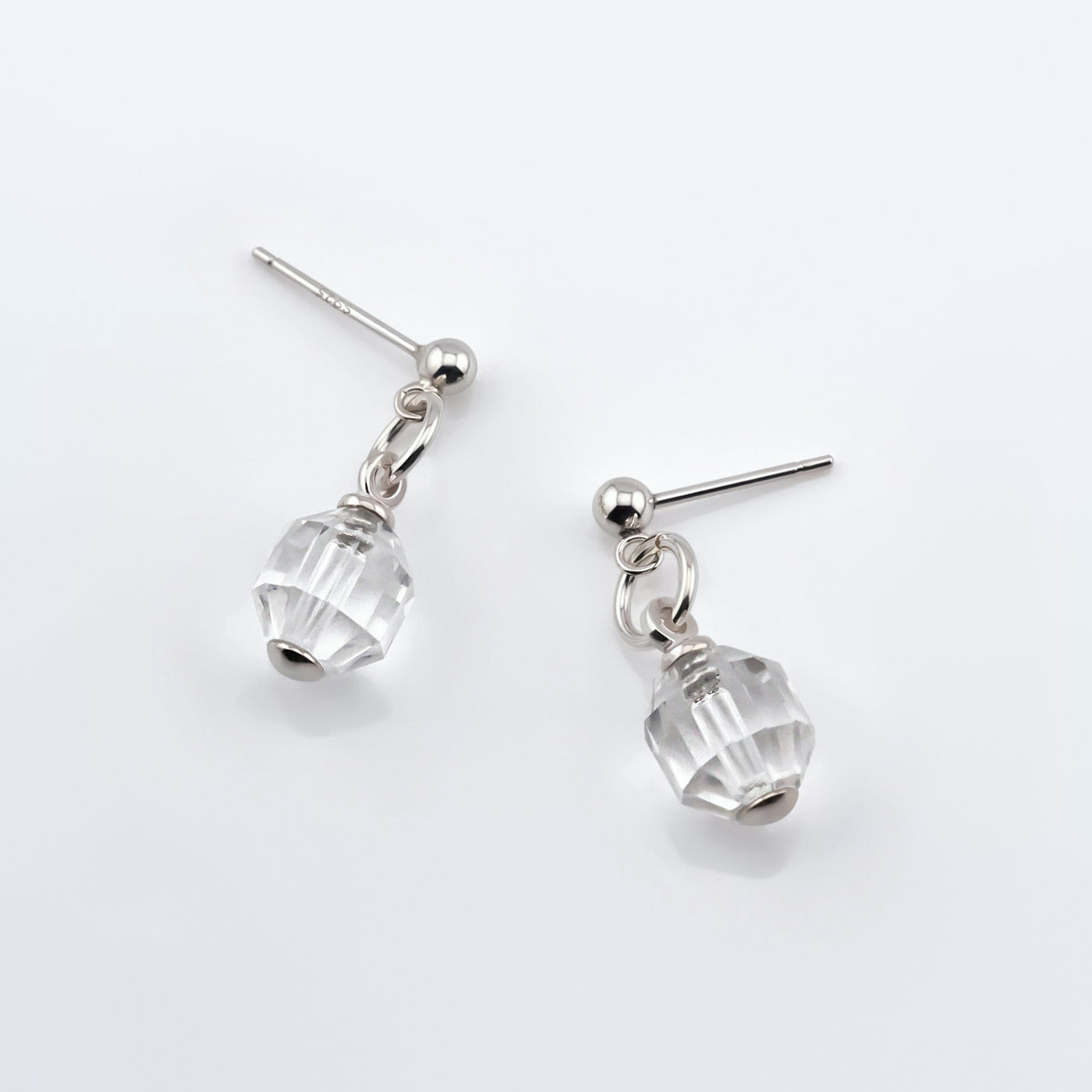 A pair of sterling silver clear quartz crystal prism earrings laying flat on a white background, top view.