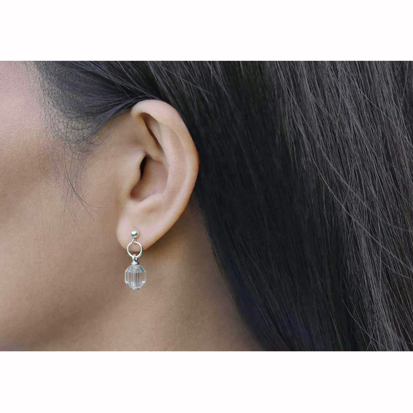 A close up of a sterling silver clear quartz crystal prism earring worn outside by a person with dark hair