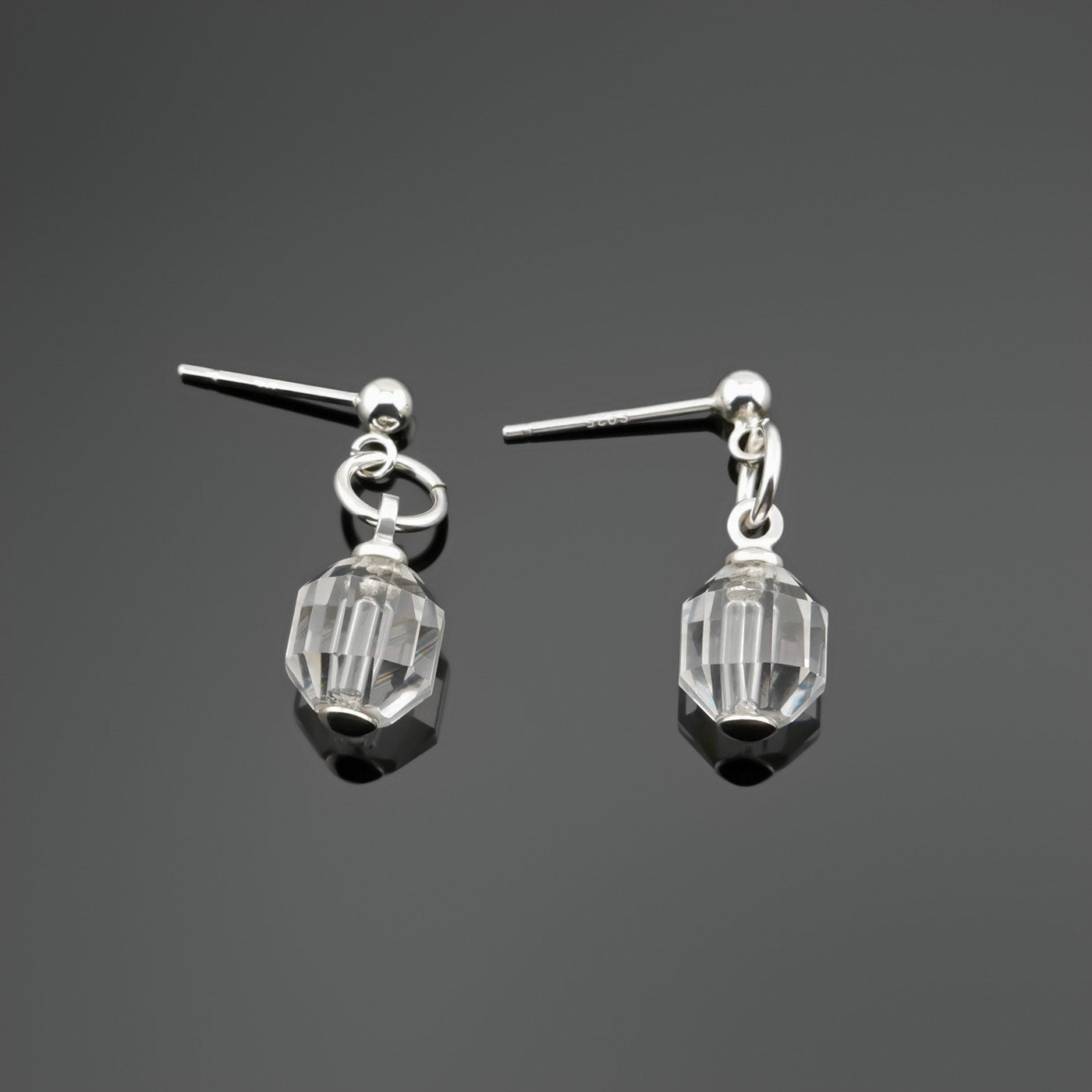 A pair of sterling silver clear quartz crystal prism earrings laying flat on a dark gray background, top view.