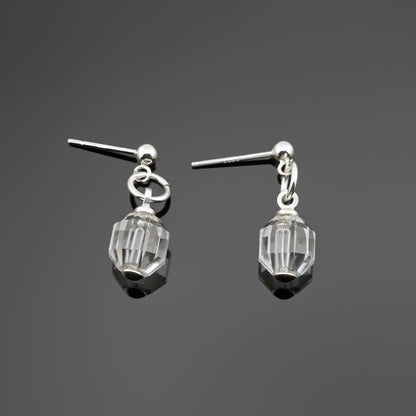 A pair of sterling silver clear quartz crystal prism earrings laying flat on a dark gray background, top view.