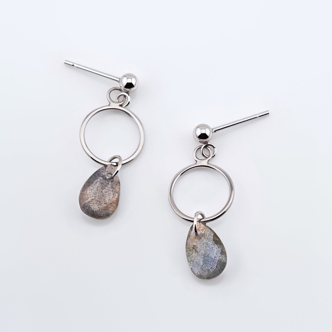 A pair of sterling silver, open circle labradorite drop earrings laying flat on a plain white background, top view.