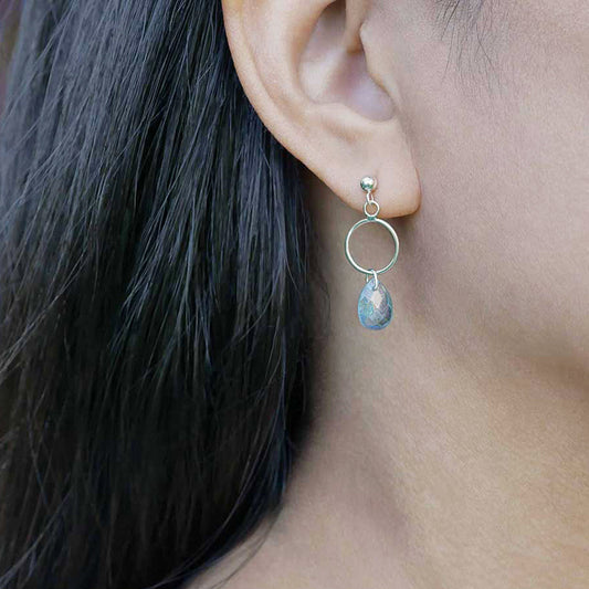 A close up of a sterling silver open circle labradorite drop earring worn outside by a person with dark hair.