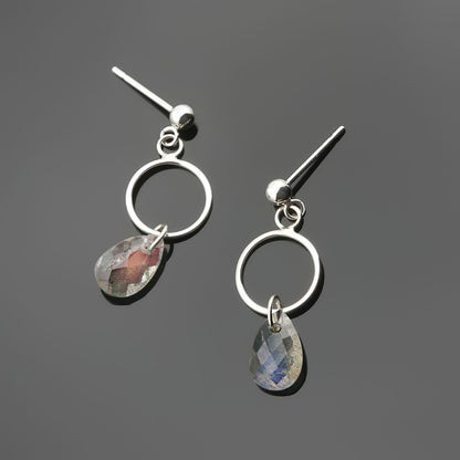 A pair of sterling silver, open circle labradorite drop earrings laying flat on a plain dark gray background, top view.