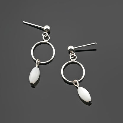 A pair of sterling silver, open circle mother of pearl MOP drop earrings laying flat on a plain dark gray background, top view.