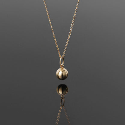 Front view of a dainty, 14k gold filled sphere ball pendant chain necklace hanging, with a plain reflective gray background.