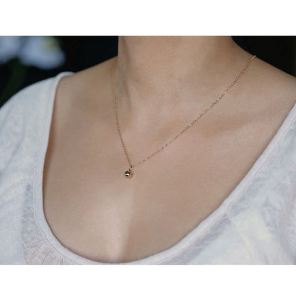 3/4 view of a dainty, round 14k gold filled sphere ball pendant necklace worn on a person wearing a light beige off white top.