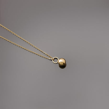 Top view of a dainty, 14k gold filled sphere ball pendant chain necklace laying flat on a plain reflective gray background.