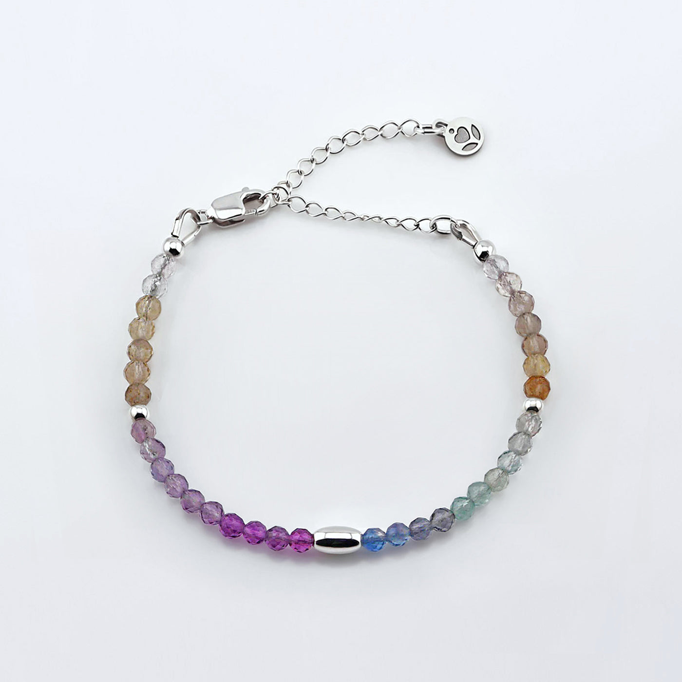Top view of a multi-colored, colorful ombre high quality AAA rainbow fluorite faceted beaded bracelet with sterling silver accent beads, clasp, reverie blossom brand logo and extender chain laying flat on a plain off white or light gray background. 