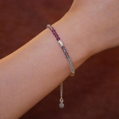 Close-up of a wrist wearing a multi-colored, colorful, ombre high quality AAA rainbow fluorite faceted beaded bracelet with sterling silver accent beads, on a brown background.