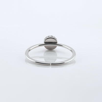Back view of a dainty adjustable sterling silver ring with a focal crown bezel setting. The ring is laying flat on a plain white reflective surface.