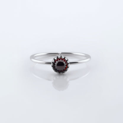Front view of a dainty adjustable sterling silver ring with a focal high quality AAA deep red hessonite garnet cabochon set in a crown bezel setting. The ring is laying flat on a plain white reflective surface.