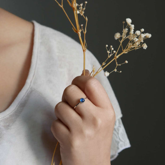 Hand holding dried baby's breath flowers with a dainty adjustable sterling silver ring with a focal high quality AAA blue kyanite solitaire gemstone cabochon set in a crown bezel setting. The person is wearing a beige off white colored top as the background.