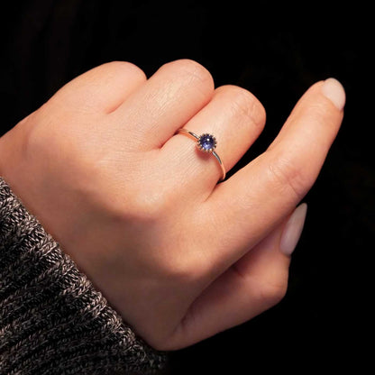 Hand wearing a dainty adjustable sterling silver ring with a focal natural high quality AAA blue kyanite solitaire gemstone cabochon set in a crown bezel setting. The person has a gray textured sleeve on with a dark black background.