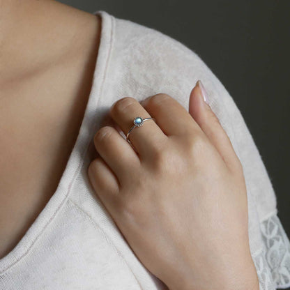 Partial view of a hand up to shoulder area of a person wearing a dainty adjustable sterling silver ring with a focal natural high quality aaa labradorite gemstone cabochon set in a crown bezel setting. The person is wearing a beige off white colored top with a dark gray background.