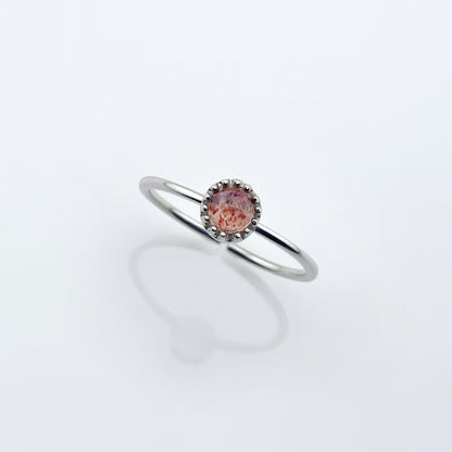 Top view of a dainty adjustable sterling silver ring with a focal strawberry quartz solitaire gemstone cabochon set in a crown bezel setting. The ring is elevated on a plain white reflective surface.