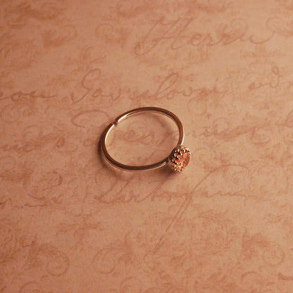 Top angle side view of a dainty adjustable sterling silver ring with a focal strawberry quartz solitaire gemstone cabochon, set in a crown bezel setting. The ring is laying flat over a textured beige pink vintage paper background with cursive writing on it.