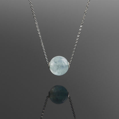 Front view of a dainty round aquaramine ball sphere pendant necklace with sterling silver 925 rivets on a sterling silver chain hanging, with a plain reflective dark gray background.