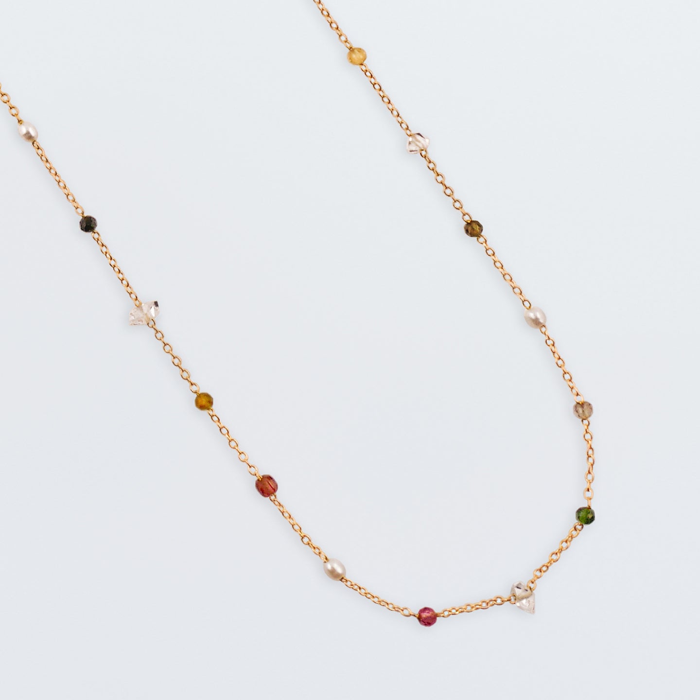Close up of Lenora high quality natural multi-colored gemstone beaded chain adjustable necklace 14K gold filled, top view with plain white background. Featuring high quality AAA Herkimer Diamond Quartz, Garnet, Rainbow Tourmaline, Natural Freshwater Rice Pearls and Smokey Quartz gemstones.