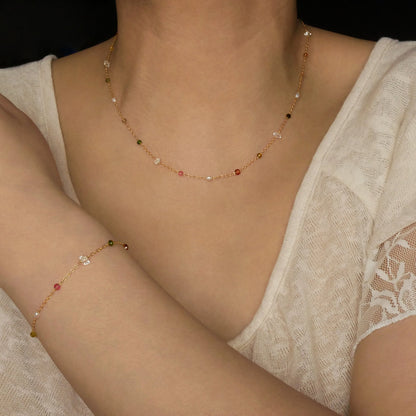 Lenora dainty high quality multi-colored gemstone beaded chain adjustable necklace and bracelet in 14K gold fill, show worn on a model's neck and wrist. Featuring high quality AAA Herkimer Diamond Quartz, Garnet, Rainbow Tourmaline, Natural Freshwater Rice Pearls and Smokey Quartz gemstones.