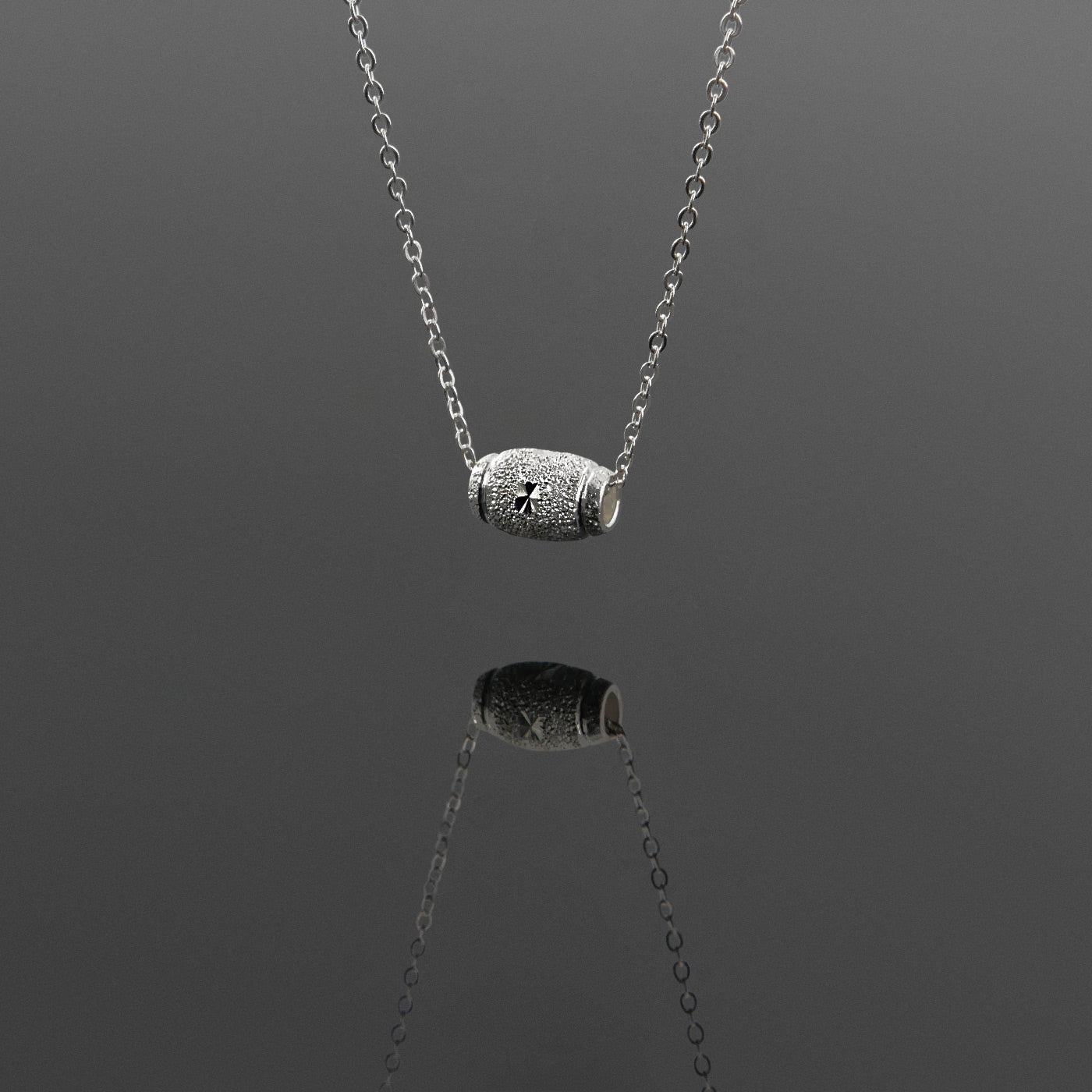 Front 3/4 view of a dainty sparkle textured barrel sterling silver pendant necklace hanging, with a plain reflective gray background.